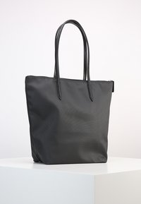 Borsa a tracolla nera con texture di tessuto liscia, manici doppi e chiusura con zip. Forma rettangolare con design minimalista e senza motivi visibili.