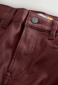 Burgundy faux leather pants with a smooth texture, featuring a metal button closure, front pockets, and contrasting stitching details.