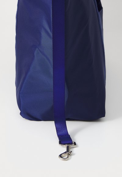 Navy blue fabric bag with a smooth texture, featuring a wide strap and a metal clip for attachment. Rounded bottom.