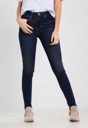Jeans skinny de color azul oscuro hechos de mezclilla, con una cintura de altura media, cinco bolsillos y una textura suave. Llevados con botas de tobillo beige.