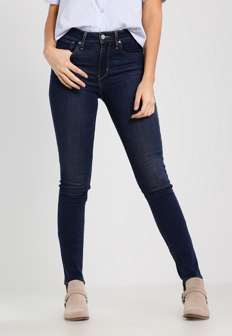 Jeans skinny de color azul oscuro hechos de mezclilla, con una cintura de altura media, cinco bolsillos y una textura suave. Llevados con botas de tobillo beige.