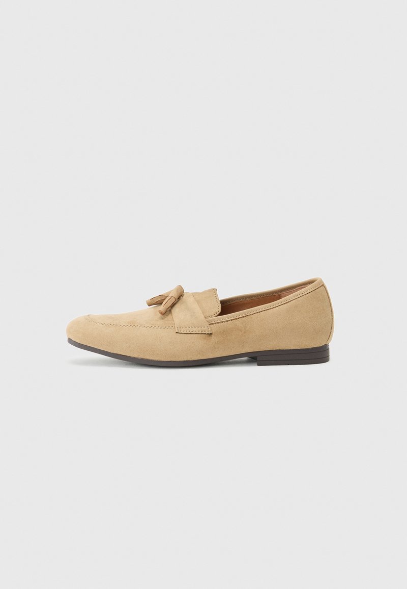 Beige Wildleder-Loafer mit einer abgerundeten Zehe, Quastenakzent und gestickten Details. Niedrige, flache braune Sohle. Einfaches Design ohne Muster.
