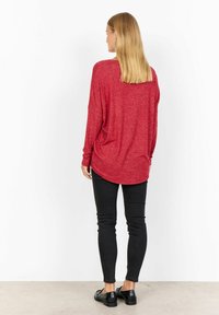 Röd långärmad topp med avslappnad passform och rundad nederkant, kombinerad med svarta skinny jeans och svarta loafer-skor. Strukturerat stickat tyg.