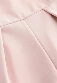 Tissu rose doux avec couture visible et détails de plis créant des plis structurés et de la texture.