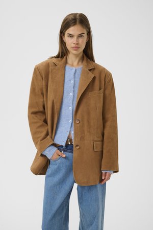 Brown suede blazer with a relaxed fit, featuring a notch lapel, two buttons, and a chest pocket, paired with a light blue knit cardigan and jeans.