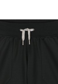 Pantaloni sportivi neri con cintura elastica, dotati di cordoncino intrecciato nero e bianco e due tasche laterali.