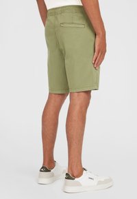 Olijfgroene shorts met een tailleband met trekkoord, één achterzak en subtiele stiksels, gecombineerd met witte en groene sneakers.