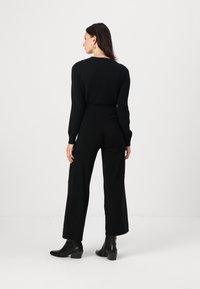 Black knitted sweater and wide-leg trousers outfit. Model wears black ankle boots. The overall look is sleek with a minimalistic design.