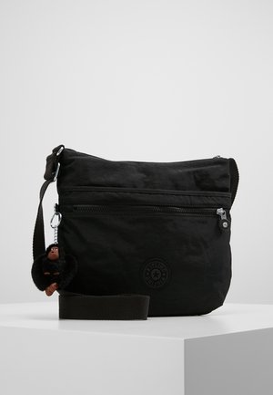Sac bandoulière noir avec poche zippée à l'avant, sangle réglable et petit porte-clés en peluche attaché sur le côté.