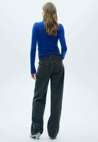 Modra dolga majica z dolgimi rokavi v kombinaciji z visoko pasom, temno sivo široko hlače. Hlače imajo dve zadnji žep in teksturiran pas.