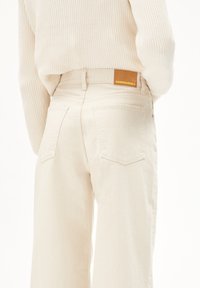 Crème-kleurige hoge taille wijde broek met een textuurafwerking, voorzien van twee achterzakken en een tan leren label op de tailleband.