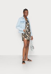 Jaqueta de denim, vestido preto floral com padrões brancos e amarelos, sandálias pretas de slide e uma bolsa cruzada cinza claro.