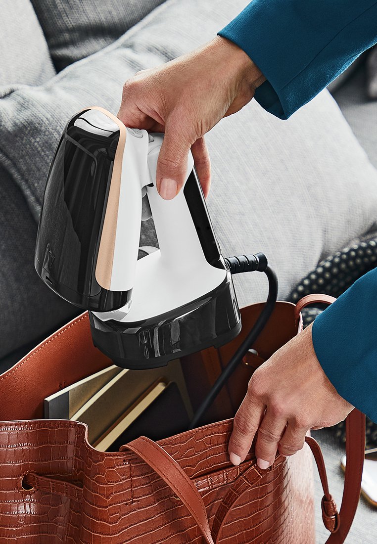 Draagbare kledingstoomgenerator met een zwart-wit lichaam, voorzien van een gladde afwerking en een gestructureerd handvat. Het wordt in een bruine leren tas geplaatst.