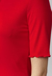 Rode ribbelshortsleeve top met een scalloped zoom; gemaakt van stretchstof en met fijne verticale lijnen voor textuur.