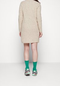 Robe en tricot beige à manches longues, avec une coupe décontractée et une texture côtelée. Assortie à des chaussettes vertes et des baskets multicolores.