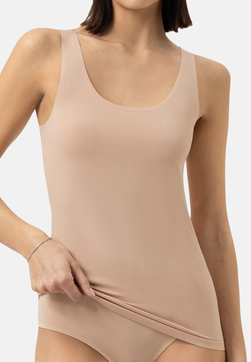 Haut sans manches beige avec un décolleté en ronde et une texture lisse, fabriqué à partir d'un matériau extensible. Accentué par un design simple et une coupe près du corps.
