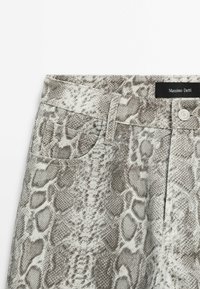 Pantalon taille haute avec motif serpent gris et blanc, fermeture à boutons devant, passants de ceinture, petite poche frontale et étiquette Massimo Dutti.