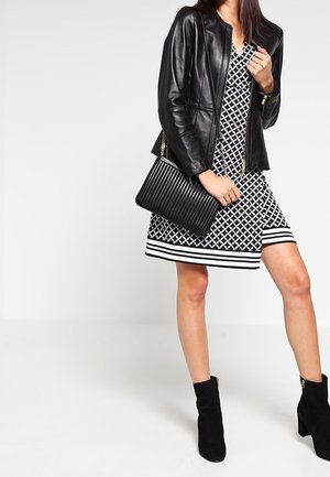 Černá kožená bunda přes černobílé šaty s proužky na lemu. Černá žebrovaná kabelka a kotníkové boty doplňují outfit.