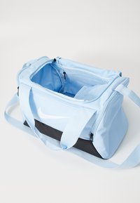 Bolsa de viaje Nike en tela azul claro con base negra. Cuenta con cierre de doble cremallera, bolsillos interiores y acento de logo en un lado.