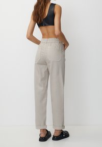 Pantalons gris clair à taille élastique avec des poignets retournés, deux poches arrière et une coupe légèrement ample, assortis d'un haut court noir.