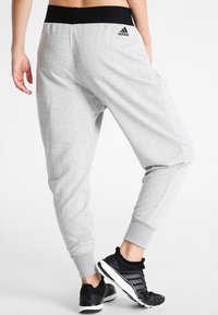Lichtgrijze joggers in een visgraatmotief, met een zwarte elastische tailleband, zijzakken en aansluitende boorden. Gekenmerkt met een zwart logo.