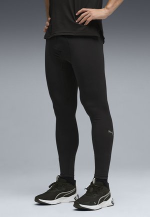 Leggings atléticos negros hechos de tela elástica con un diseño ajustado, que presentan un pequeño logotipo de Puma en la parte inferior de la pierna y combinados con zapatos atléticos negros.