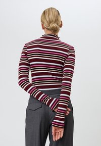 Langs mouw gestreepte top in bordeauxrood, crème en roze met een aansluitend ontwerp en uitlopende mouwen, gedragen met grijze high-waisted broek.