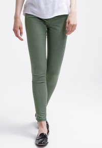 Vihreät kapeat farkut, jotka on valmistettu joustavasta kankaasta, ja niille on ominaista sileä pinta ja istuva muotoilu. Yhdistetty mustiin, kiiltäviin loafereihin.