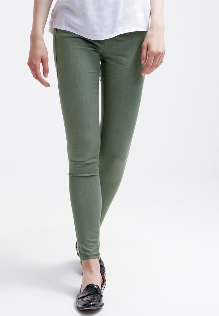 Vihreät kapeat farkut, jotka on valmistettu joustavasta kankaasta, ja niille on ominaista sileä pinta ja istuva muotoilu. Yhdistetty mustiin, kiiltäviin loafereihin.