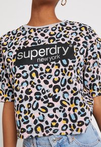 Kratký tričko s leopardím potiskem a logem "superdry new york", nošené s světle modrými džíny a zlatými kruhovými náušnicemi.