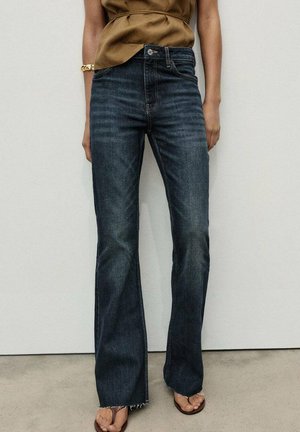 Jeans a palazzo blu scuro con vita alta. Il materiale è denim con una finitura leggermente sbiadita. Presenta un orlo grezzo e tasche frontali.