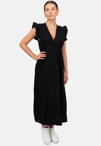 Zwarte, middellange jurk met een V-hals, gerimpelde mouwen en een geplooide taille. G gedragen met witte sneakers. Textuurstof.