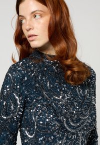 Robe bleu marine en velours avec des embellissements en sequins et perles complexes en motifs tourbillonnants, col montant et manches longues.