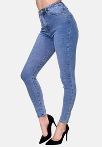 Jeans skinnys de denim azul con una cintura alta, silueta ajustada, bolsillos en la parte delantera y un acabado limpio. Combinados con unos tacones de aguja negros.