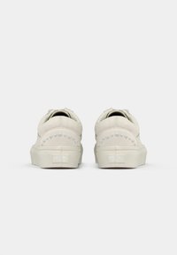 Λευκά αθλητικά παπούτσια με μαλακή υφή, διακοσμημένα με μικρέ�ς ασημένιες τρουκς κατά μήκος της πλάτης. Στρογγυλεμένο σχέδιο με χαμηλό προφίλ και ενισχυμένη φτέρνα.