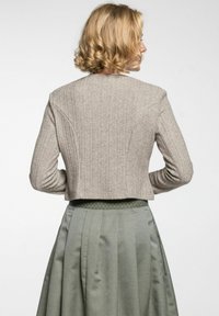 Beige gestrickte cropped Jacke mit geripptem Material und detailliertem Muster, kombiniert mit einem grünen strukturierten Rock mit Rautenmuster.