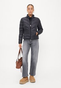 Zwarte pufferjack met verticale en chevron quilting, met ritssluiting, gedragen over een zwart shirt. Gecombineerd met grijze jeans en bruine plateau laarzen.