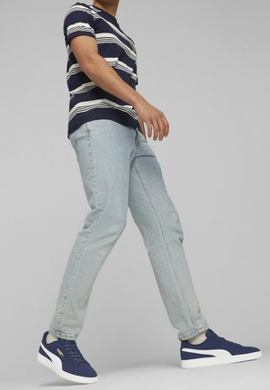 T-shirt a righe blu navy, jeans azzurri chiari e sneakers blu navy con dettagli bianchi; il tessuto sembra un misto cotone con una vestibilità casual e una texture morbida.