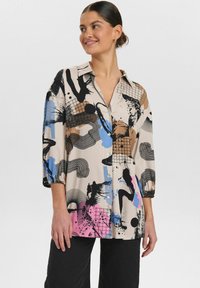 Chemisier col montant beige clair avec des motifs abstraits bleus, bruns, roses et noirs. Doté de manches trois-quarts et d'une coupe ample.