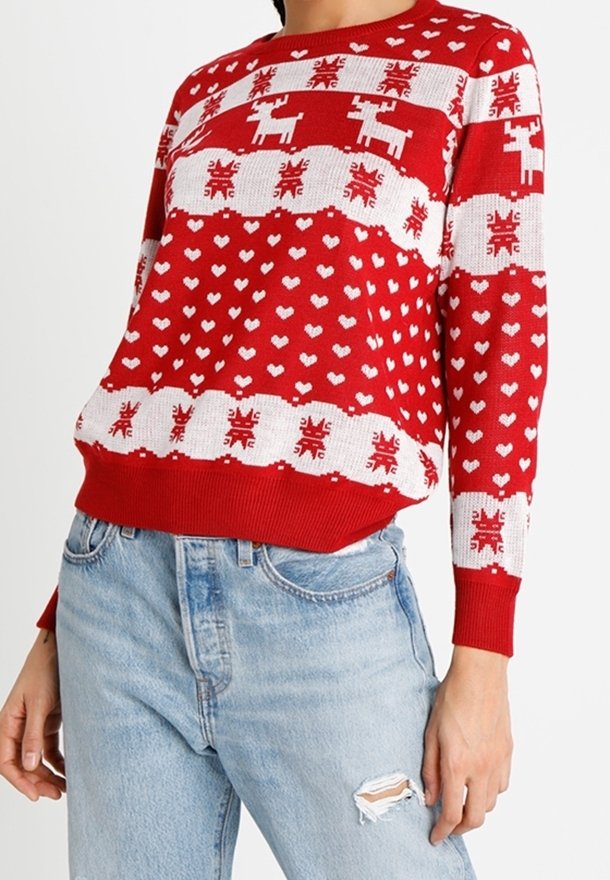 Pull en tricot rouge avec des motifs de rennes et de cœurs blancs, des poignets et un ourlet côtelés, et une coupe décontractée. Porté avec un jean en denim usé.