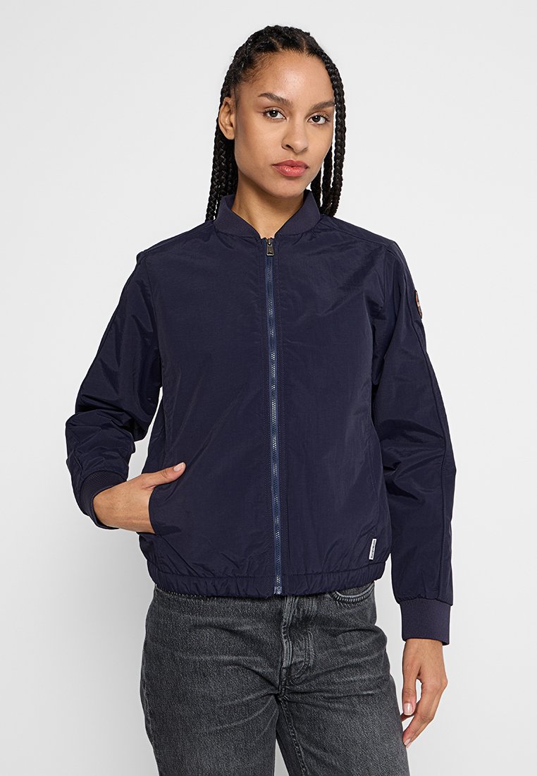 Giacca bomber blu navy con chiusura a zip frontale, polsini a costine e colletto rialzato. Presenta una discreta toppa con logo sulla manica. Tessuto liscio.