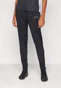 Svarte treningbukser laget av lette materialer, med slim fit, elastisk midje og en hvit Nike-logo på venstre lår.