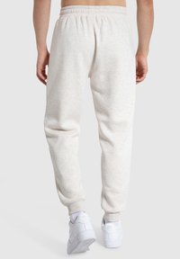 Hellgraue Jogginghosen mit elastischem Bund, schmaler Passform und weichem Material, kombiniert mit weißen Sportschuhen.