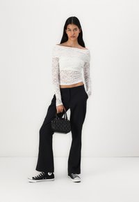Haut en dentelle blanche à épaules dénudées, pantalon noir à jambes larges, sac à main noir avec un design texturé et baskets Converse noires.