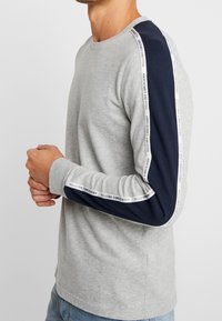 Langarm T-shirt van grijze katoen met marineblauwe mouwen, featuring zijstrepen met de tekst "Abercrombie and Fitch". Klassieke ronde hals.