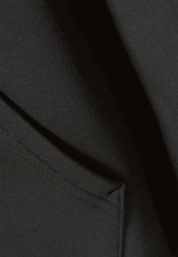 Țesătură de material negru cu textură netedă văzută în prim-plan, prezentând un buzunar înclinat cu cusături îngrijite și strălucire ușoară.