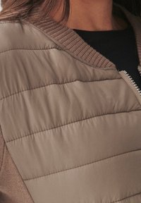 Giubbotto puffer marrone chiaro, con sezioni trapuntate, colletto a costine e tessuto liscio con chiusura frontale a zip.