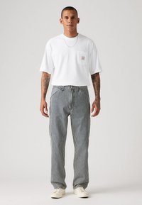 Camiseta de algodón blanca con un bolsillo en el pecho, combinada con pantalones de rayas azul y blanca y zapatillas blancas. Diseño sencillo y corte relajado.