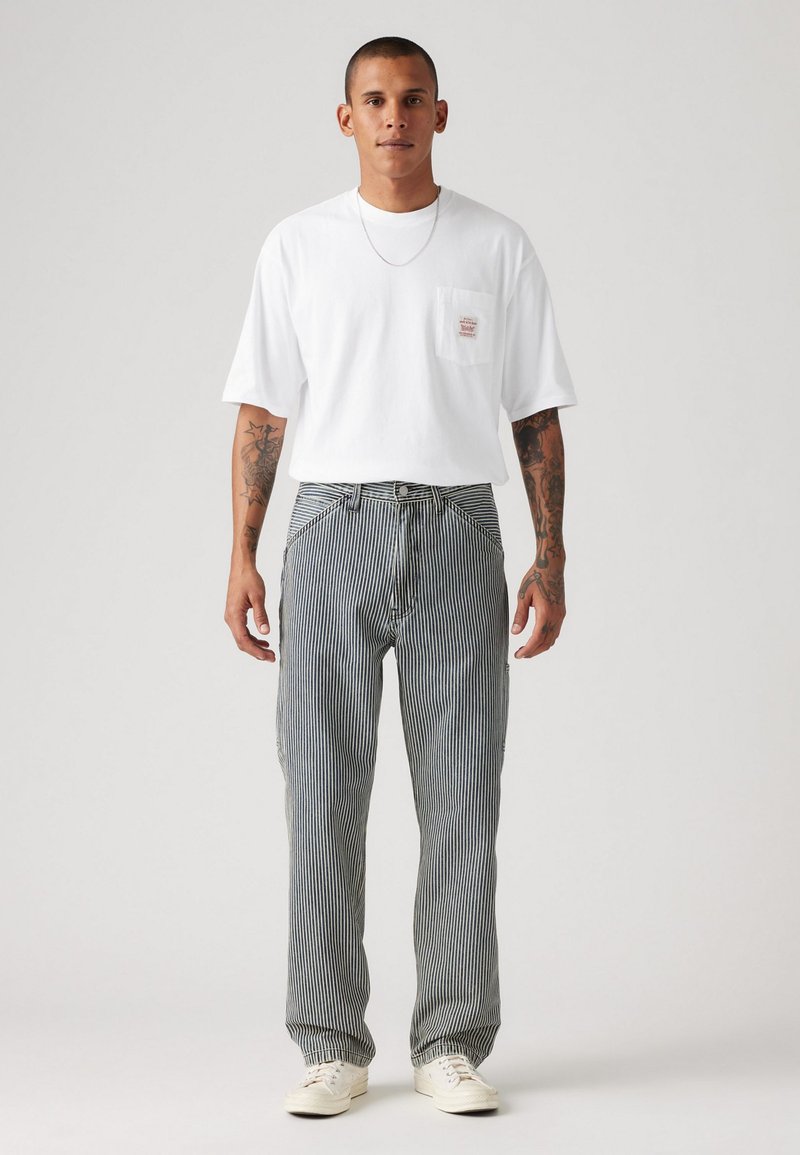 Camiseta de algodón blanca con un bolsillo en el pecho, combinada con pantalones de rayas azul y blanca y zapatillas blancas. Diseño sencillo y corte relajado.