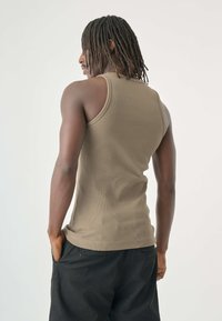 Khakifarbene, gerippte Tanktop mit figurbetontem Design, rundem Ausschnitt und breiten Trägern, kombiniert mit lockeren schwarzen Hosen.